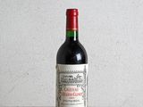 bottle of red wine sitting on a wooden table with a white wall in the background