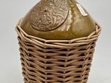 une photo représentant un vase marron muni d'un couvercle, placé dans un panier en osier