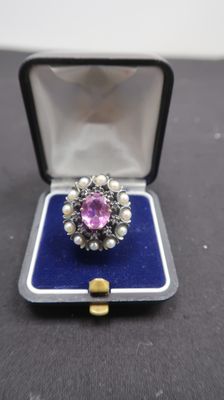 une photo d'une bague dans un écrin, avec des perles et une pierre rose