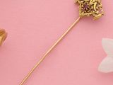 une image représentant une broche en or ornée d'une fleur sur fond rose