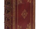 un vieux livre rouge avec des bordures dorées posé sur une surface blanche