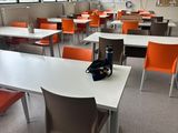 Il y a de nombreuses tables et chaises dans cette salle de classe, avec une horloge accrochée au mur.