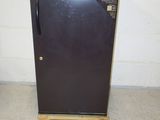 a small black refrigerator in a room with a white brick wall