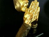 statue of a praying hand with a gold face on a black base