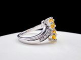 a close up of a yellow sapphire and diamond ring on a white surface