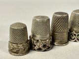 four antique thimbles are lined up in a row on a white surface