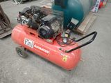 a red air compressor sitting on the ground next to a blue tank