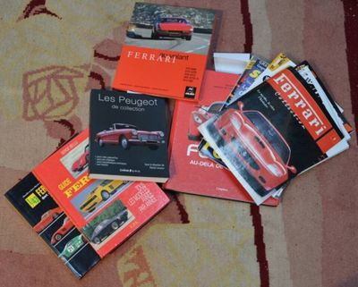 plusieurs livres posés sur un tapis, avec une voiture rouge en arrière-plan