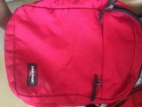 Quelqu'un tient un sac à dos rouge posé par terre.