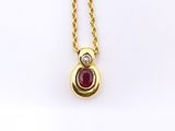 a close up of a gold necklace with a ruby and diamond pendant