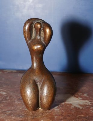 sculpture représentant une figure féminine posée sur une table, avec l'ombre d'une personne en arrière-plan
