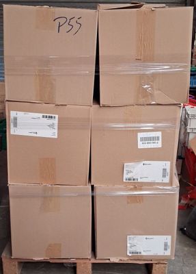 plusieurs cartons empilés sur une palette dans un entrepôt, avec une personne à l'arrière-plan