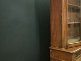 a tall wooden cabinet with a glass door on top