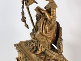a gold clock with a woman sitting on top of it