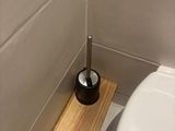 a toilet with a toilet brush in the corner of the bathroom
