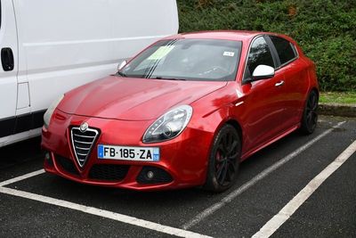 une voiture rouge garée sur un parking à côté d'une camionnette blanche