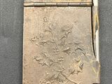 a small silver cigarette case with a pen on it