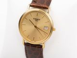 a gold watch on a brown leather strap on a white pillow