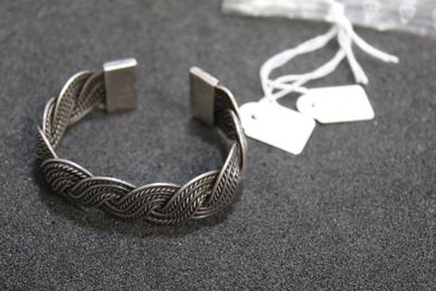 silver bracelet with braid design on a black surface with a tag on it