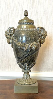 un vase en argent posé sur une table en bois, avec un mur blanc en arrière-plan
