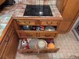 une cuisine avec des placards en bois et une plaque de cuisson sur laquelle sont posées des casseroles et des poêles