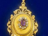 a close up of a gold pendant with a purple stone in the center