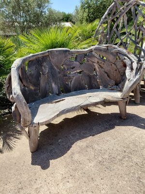 a bench made out of drift wood in the middle of a garden