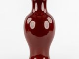 un vase rouge posé sur une surface blanche