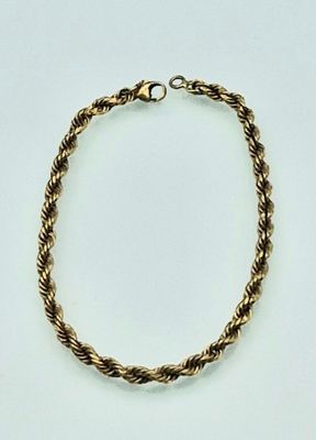 a close up of a gold rope bracelet on a white surface