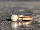 a gold ring with a pearl on it on a table
