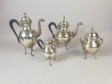 four pieces of silver tea and coffee set on a white surface