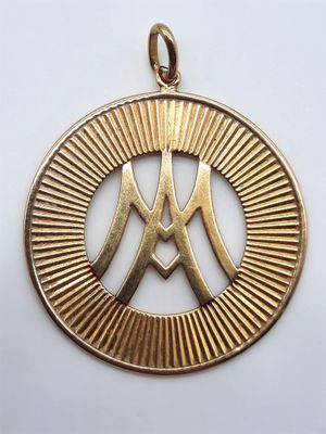 un pendentif en or représentant la lettre « m » dans un cercle, entouré de rayons