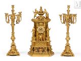three gold colored candlesticks and a clock on a white background