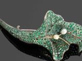 une image représentant une broche verte ornée d'une perle et de feuilles vertes