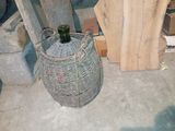un panier en osier posé par terre, contenant une bouteille de vin
