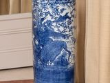 un vase bleu et blanc posé par terre devant un rideau