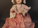a doll that is sitting on the ground wearing a pink dress