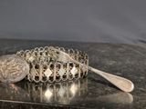 a silver bracelet with a coin and a spoon on a table