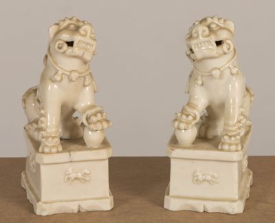 pair of white ceramic foo foo statues sitting on top of a wooden table