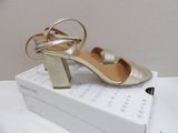 silver and gold high heeled sandals on a box on a white surface