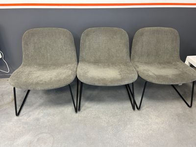 three grey chairs with black legs in front of a gray wall