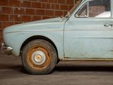 an old blue car parked in front of a brick wall