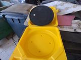 Quelqu'un tient un objet jaune dans la main, devant un tas de vieilleries.
