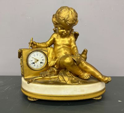 une statue en or représentant un enfant, avec une horloge posée sur une table