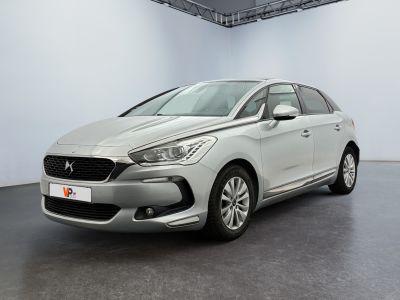 Une voiture argentée est garée dans une pièce blanche au sol noir.