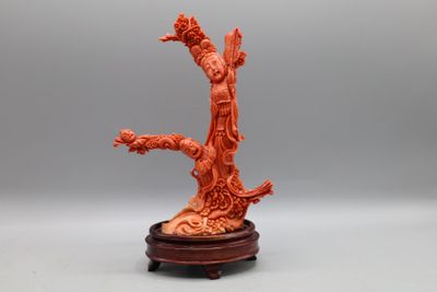 une sculpture orange représentant une femme tenant un oiseau, posée sur un socle en bois
