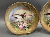 pair of decorative plates with birds painted on them sitting on a table