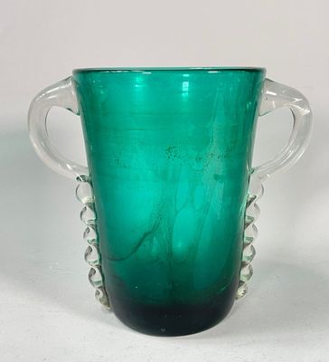 un vase en verre vert muni de deux anses, posé sur une surface blanche
