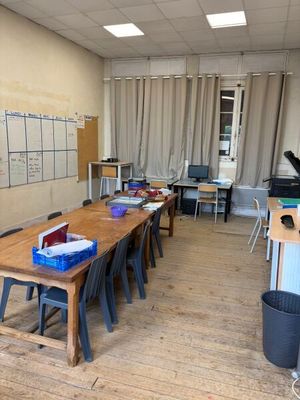 des tables et des chaises dans une salle de classe avec un tableau blanc accroché au mur