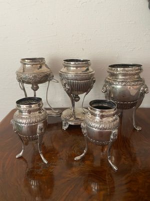 five silver vases sitting on a table with a clock in the background